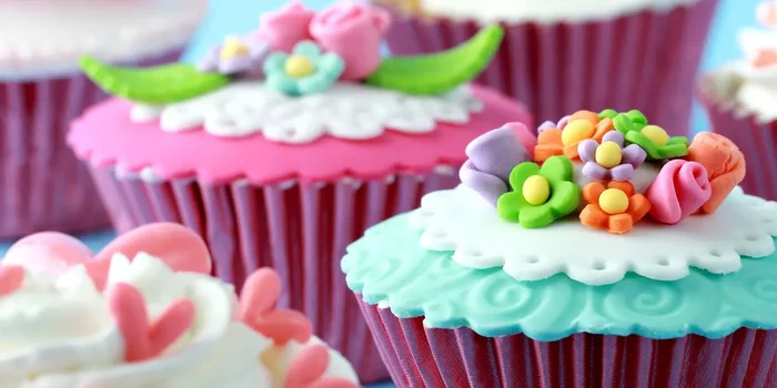 Mit Fondantdecke überzogene und mit Blüten aus verschieden farbigem Fondant dekorierte Cupcakes