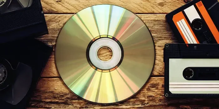 Eine CD und mehrere Kassetten liegend auf einer rauen Oberfläche aus Holz