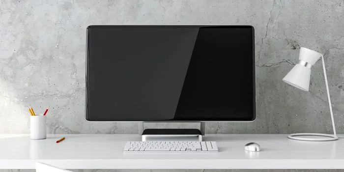 Ein PC mit abgerundeten Ecken, schwarzem Bildschirm und einer weißen Tastatur sowie PC-Maus steht auf einem weißen Schreibtisch vor einer marmorierten Wand