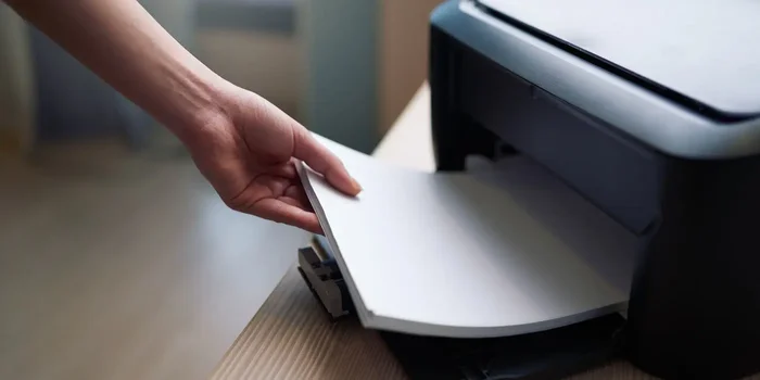 Frauenhand, die Papier in den Einzug eines Druckers einlegt