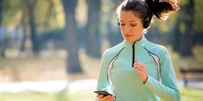 Junge Frau mit Kopfhörern und Smartphone in der Hand beim Joggen in einem Park