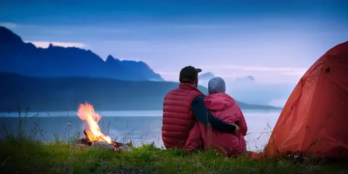Paar sitzt neben einem Lagerfeuer und blickt auf einen See