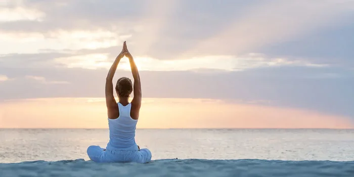 Frau macht Yoga-Übungen am Strand. Im Hintergrund ist der Sonnenuntergang zu sehen