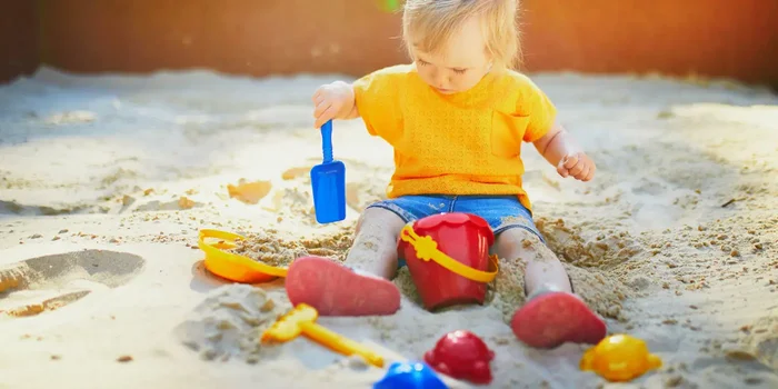 Kind spielt im Sandkasten mit Spielgeräten