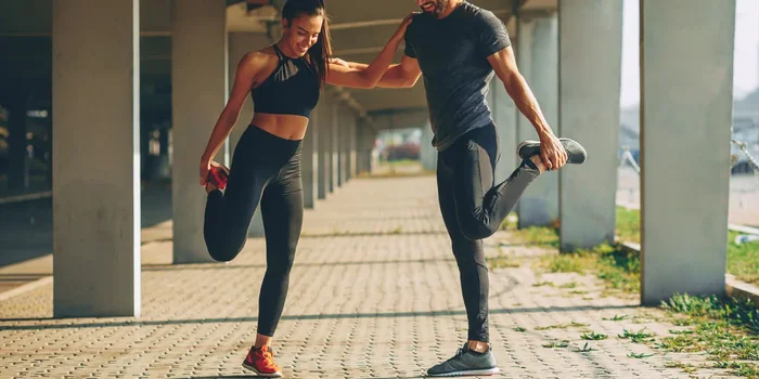 Mann und Frau tragen funktionelle Sportkleidung, während sie Dehnübungen machen