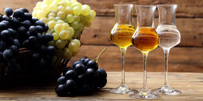 Drei verschiedene Schnäpse in einem Nosingglas stehen neben Weintrauben