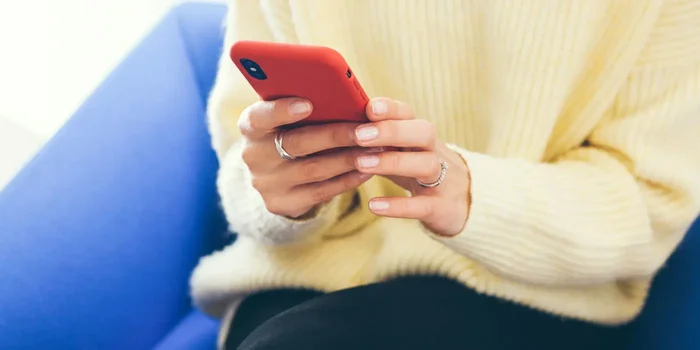 Frau sitzt auf einem Sofa und hält ihr Handy in roter Schutzhülle in der Hand