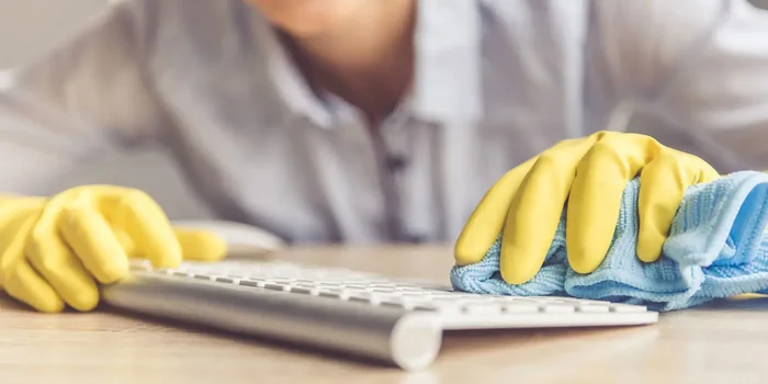 Junge Frau mit Gummi-Handschuhen wischt mit einem Lappen über eine Tastatur