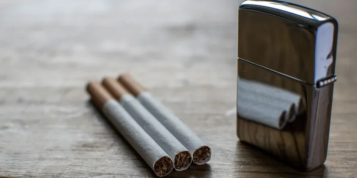 Geschlossenes Zippo steht neben drei Zigaretten auf einem Holztisch.