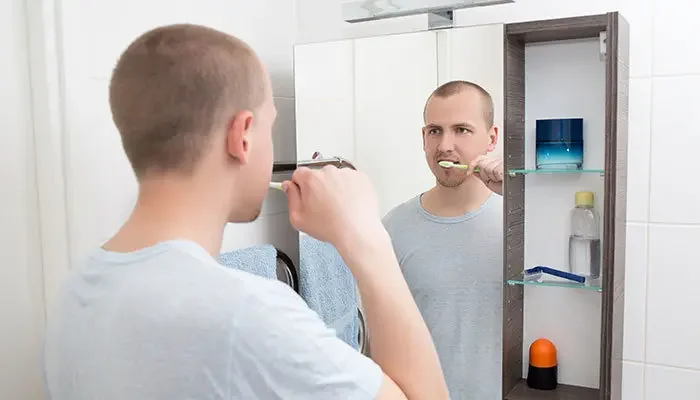 Aufnahme eines Mannes, welcher sich vor einem Spiegelschrank die Zähne putzt.