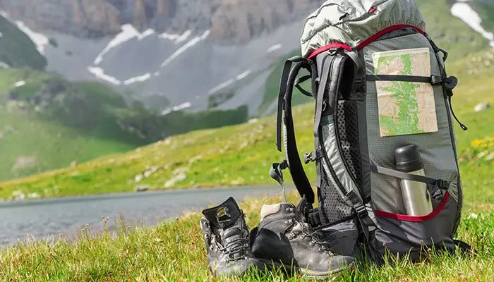 Trekking-Rucksack steht neben Wanderschuhen auf der Wiese einer Berglandschaft